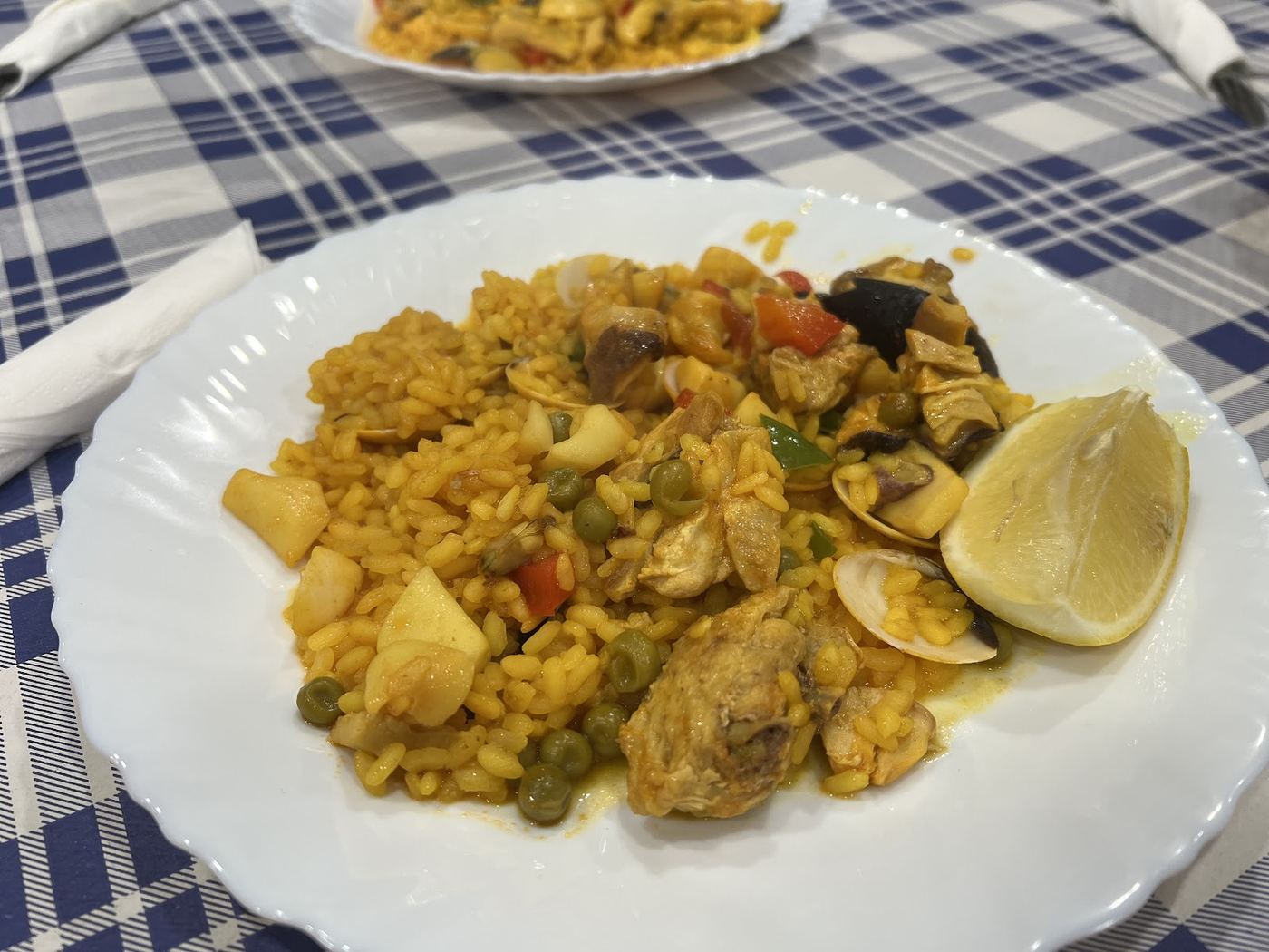 Paella mixta servida en paellera, con arroz, carne, marisco y un gajo de limón.
